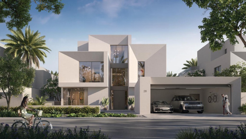 Moderne 5-Schlafzimmer-Villa in Mirage at the Oasis von Emaar, Dubailand. Die luxuriöse Immobilie besticht durch eine minimalistische Architektur mit klaren Linien, großen Glasfenstern und einer eleganten Fassade. Die Villa verfügt über eine Doppelgarage mit hochwertigen Fahrzeugen, eine einladende grüne Umgebung und einen stilvollen Eingangsbereich mit hohen Decken und Designer-Beleuchtung. Perfekt für anspruchsvolle Käufer, die eine exklusive Immobilie in Dubai suchen. Jetzt auf nikvandamme.ae entdecken.